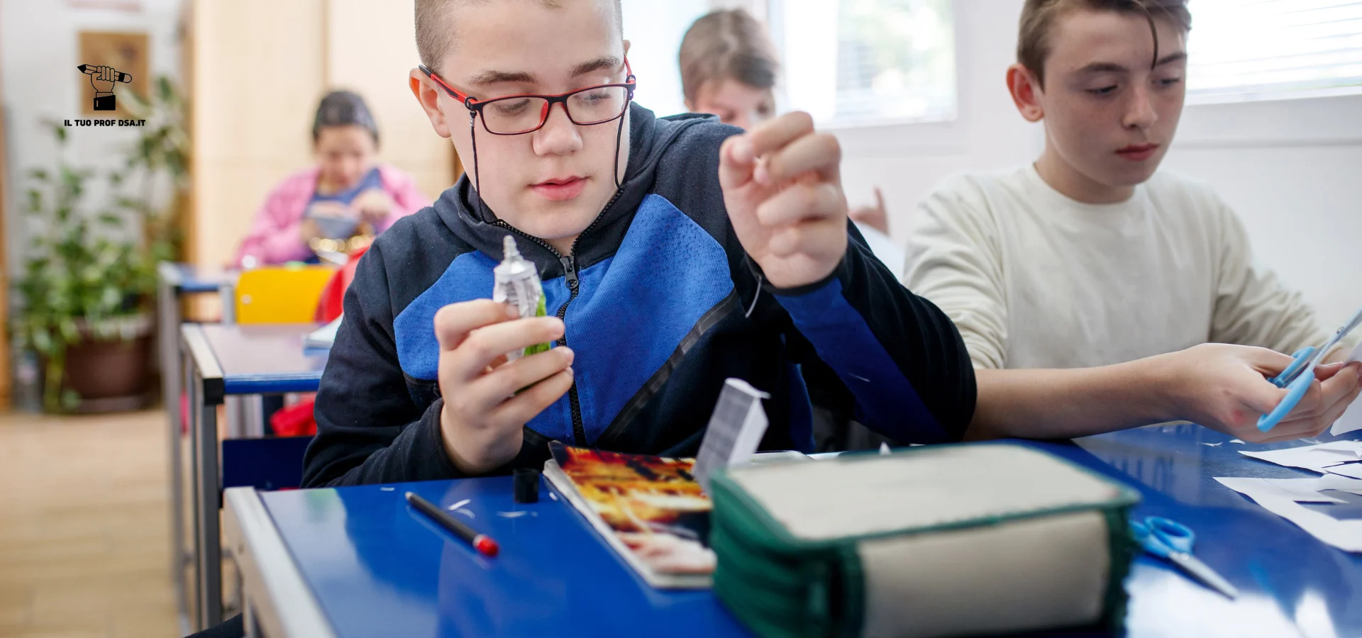Studente in classe con occhiali e supporto visivo al collo mentre svolge un’attività manuale al banco, in un contesto scolastico legato ai disturbi specifici dell’apprendimento.
